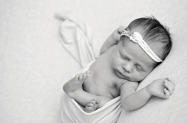 Black and white photo of newborn baby girl with headband.