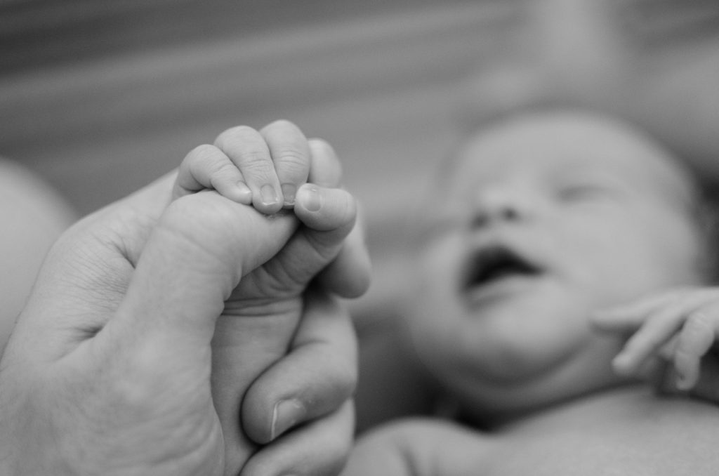 Newborn baby grasps onto mothers hand.