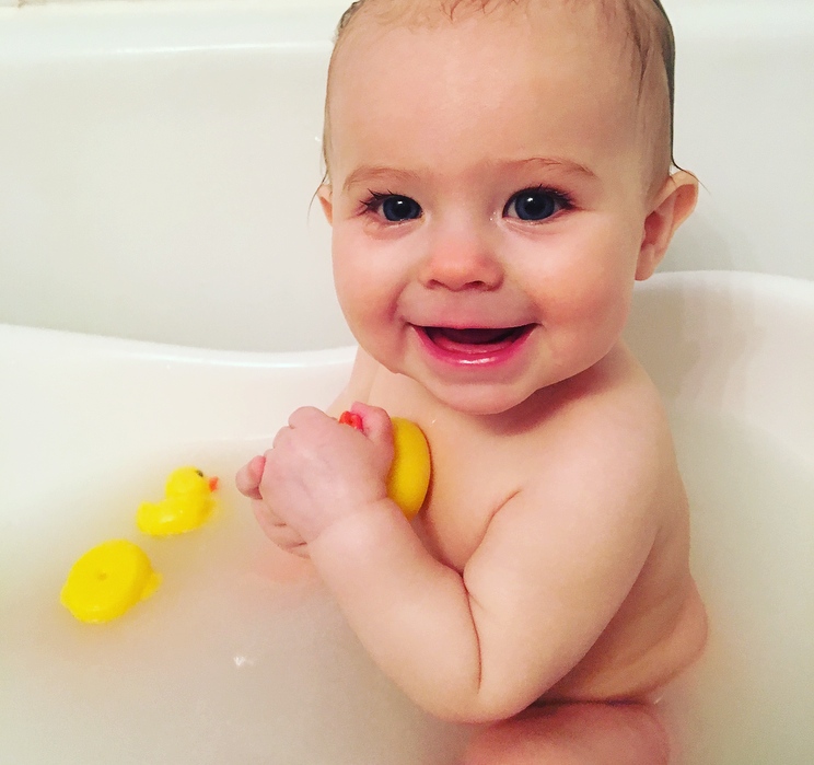 Baby plays in tub with rubber duckies.