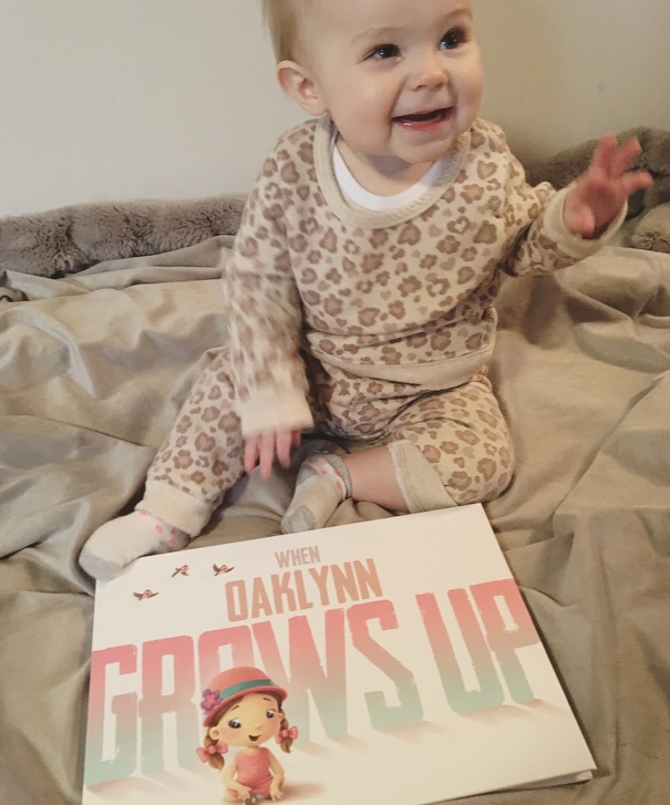 Little girl sits on bed with book, personalized with her name.