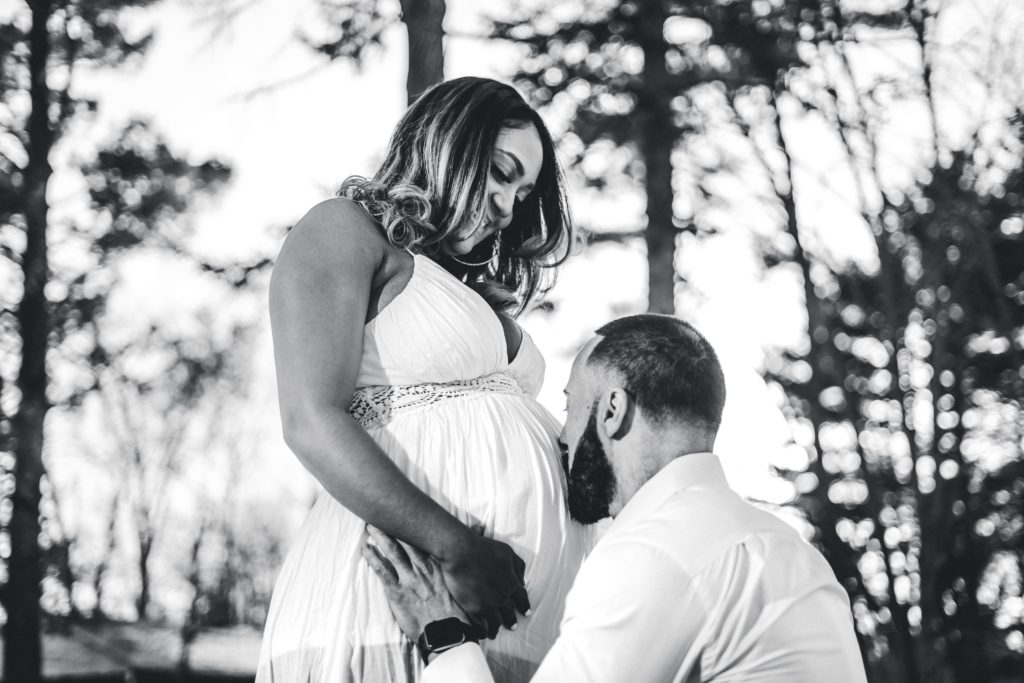 Black and white photo of pregnant woman and man kissing belly.