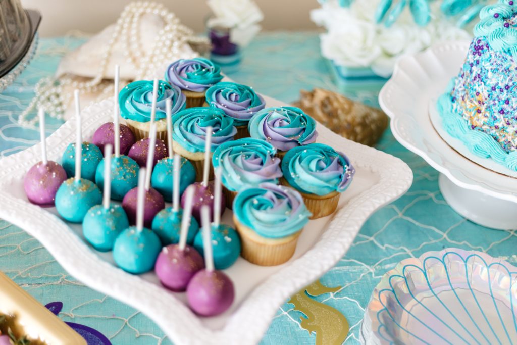 Purple and blue cupcakes and cupcake bites on party table.