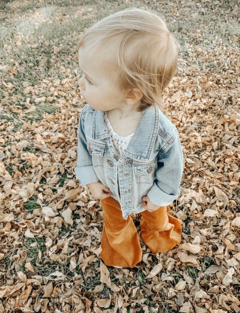 Little girl plays outside in denim jacket and copper colored pants.