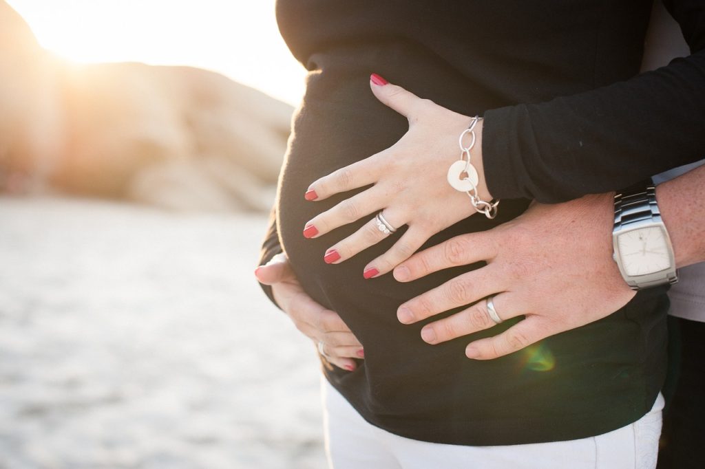Couple cradles woman's pregnant belly on beach.