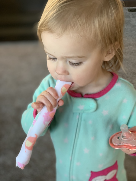 Toddler girl eats yogurt from tube.