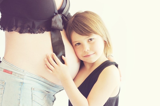Young girl hugs mother's pregnant belly.